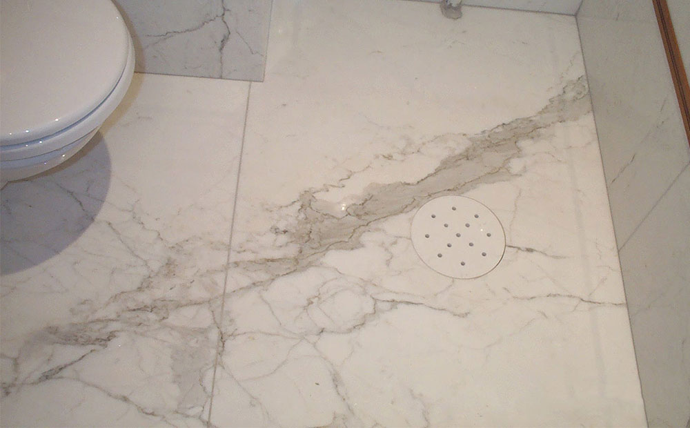 Badrumsgolv i dusch av marmor med åderföljning och golvbrunn i marmor