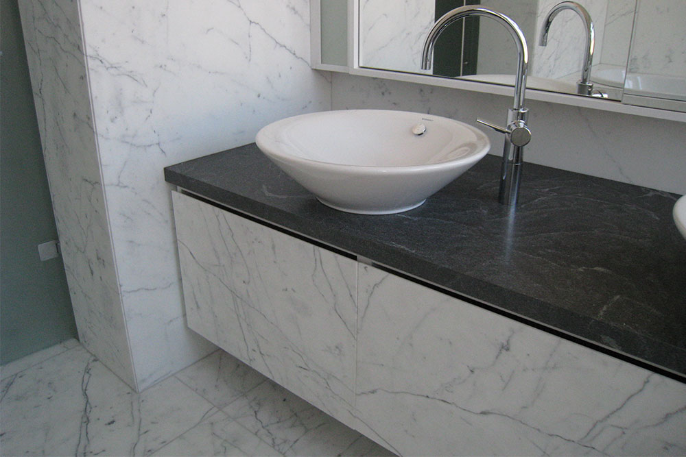 Svart granitbänkskiva med vita marmorväggar och marmorgolv i badrum